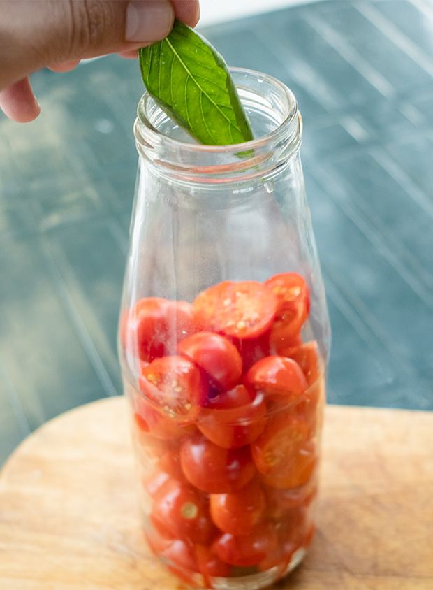 Hand putting basil inside the bottle of cherry tomatoes