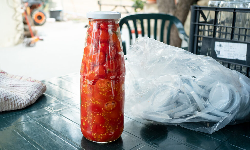 A sealed bottle of tomatoes with a packet of caps beside it